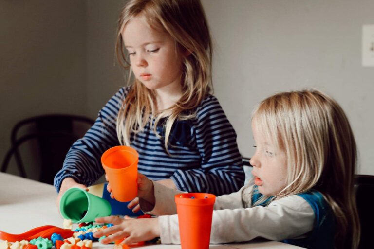 Two little girls playing with orange cups at the table